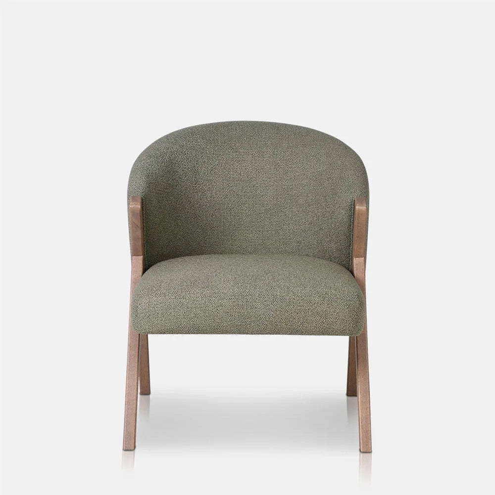 Lyndon Curved Accent Chair in pistachio has a rounded green upholstered back and padded seat, supported by a warm wooden frame with gently angled legs.