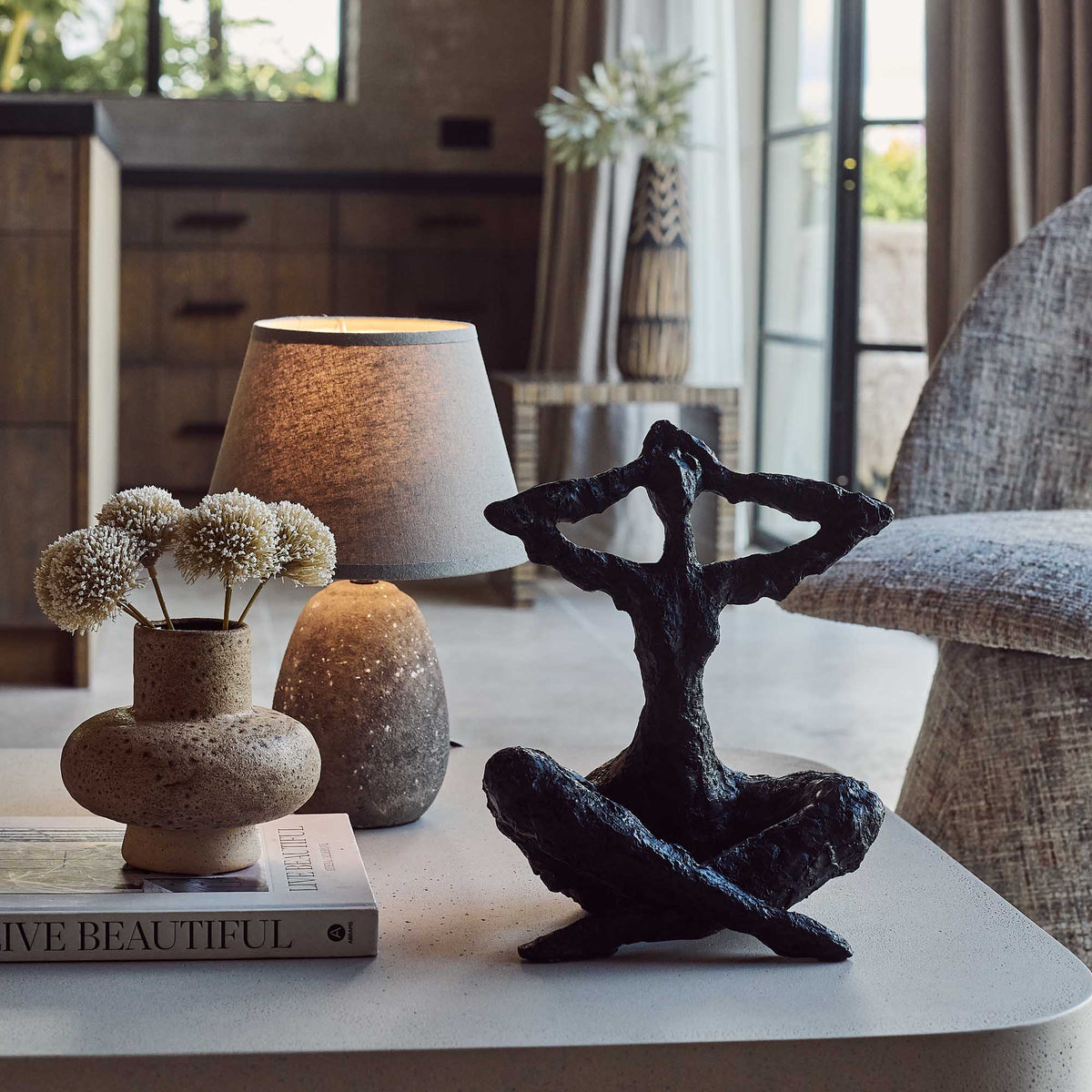 Decorative items on a table including a black sculpture, vase with flowers, and book in a living room setting.