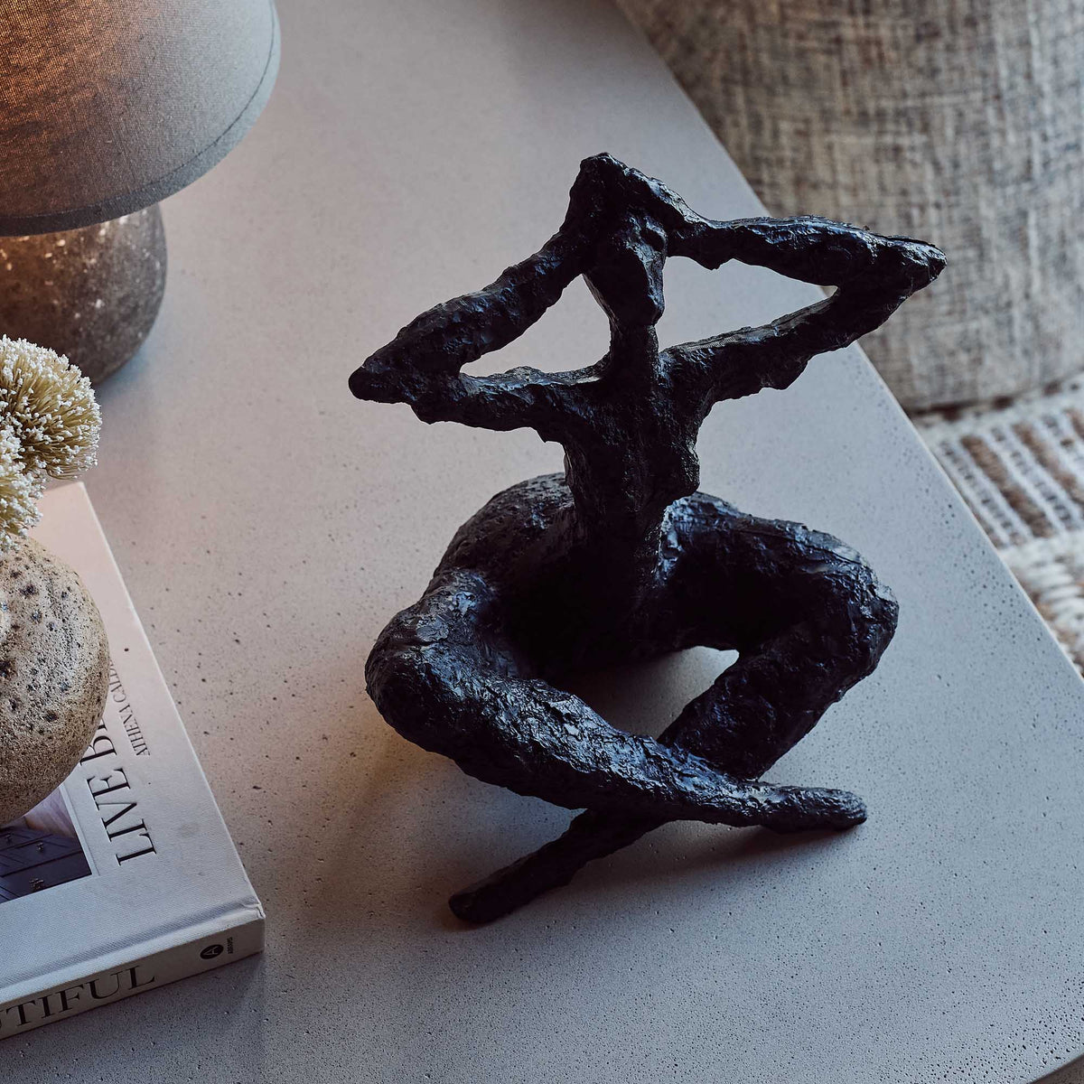 Black abstract sculpture on a textured surface with a magazine and decorative items.