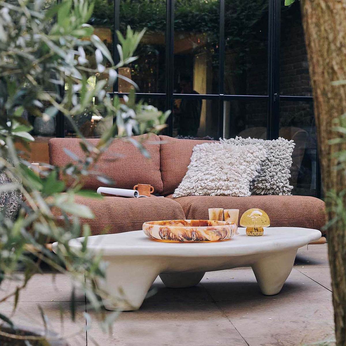 Cream stone effect coffee table with a sculptural round design, curved silhouette and textured organic finish. Medina Coffee Table by Abigail Ahern, featuring a contemporary shape and neutral tones that create an elegant centrepiece for modern living rooms and luxury interiors. A statement designer coffee table perfect for styling with decorative accessories, books and lighting, adding natural texture and timeless sophistication to your home decor.
