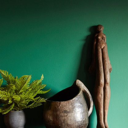 Bold rich green painted wall behind a tall sculpture and artificial green fern