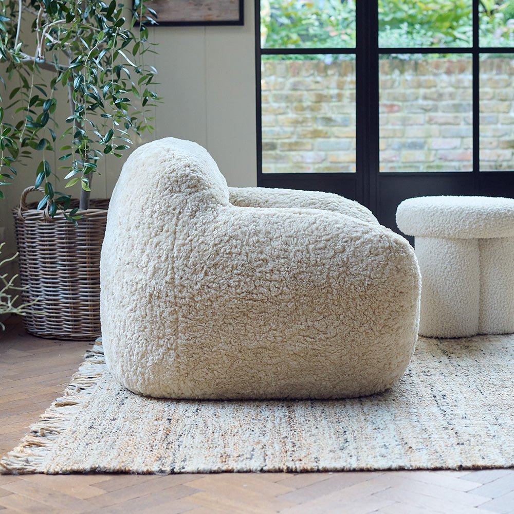 The Monroe Faux Shearling Armchair, an oversized cosy tub style chair in cream, on a neutral toned rug in a light airy room.
