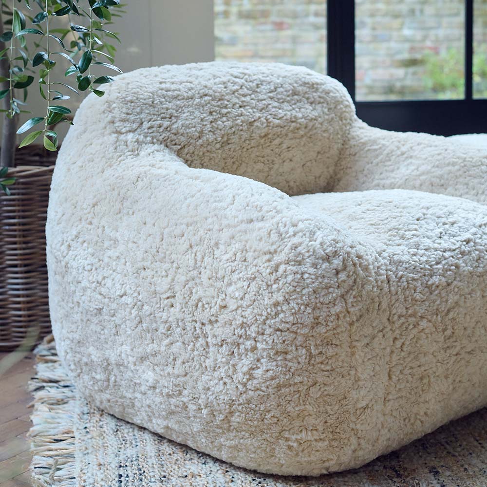 The Monroe Faux Shearling Armchair, an oversized cosy tub style chair in cream, on a neutral toned rug in a light airy room.