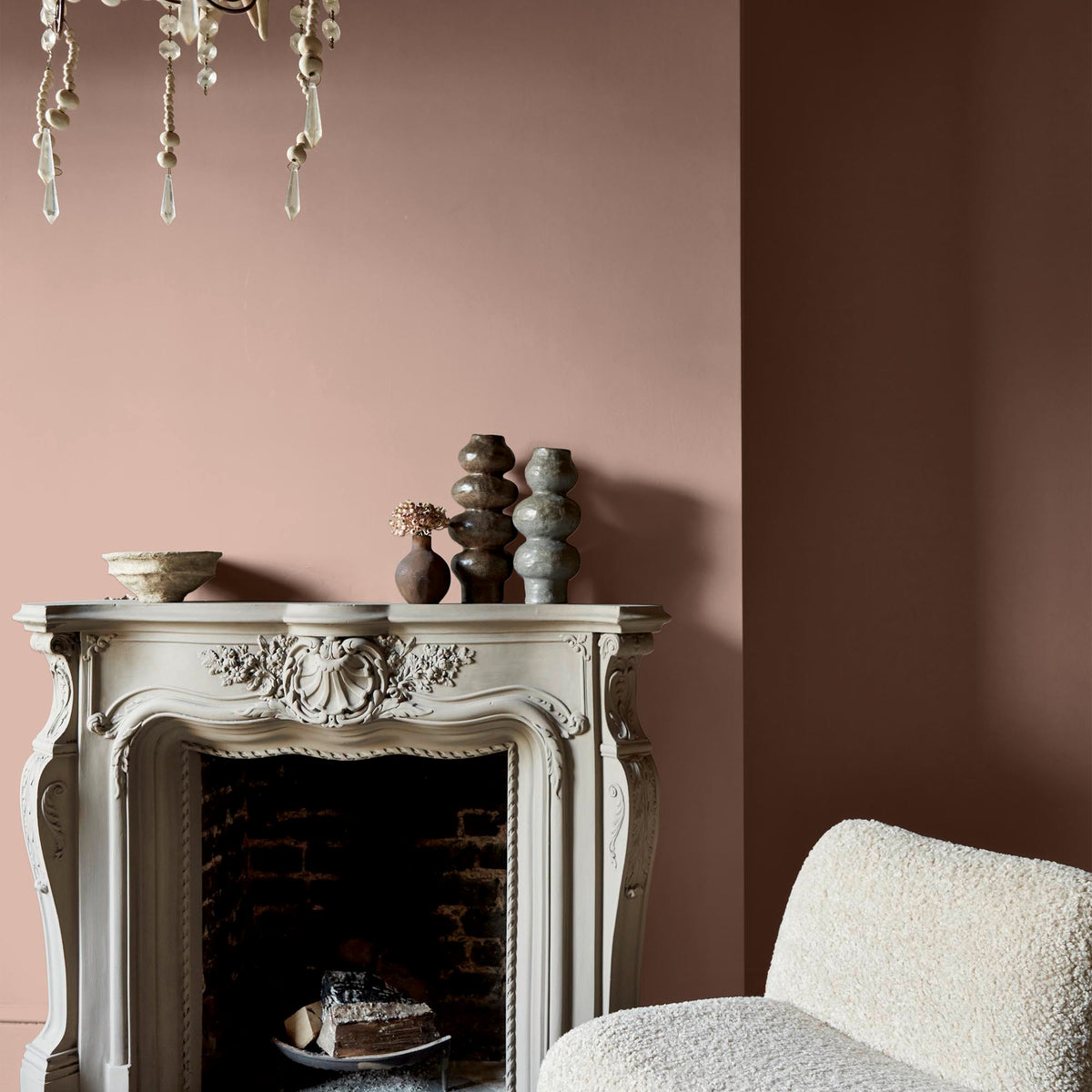 A fireplace with ceramic vases with an accent chair in front, the walls are painted in a warm, blush pink paint colour.