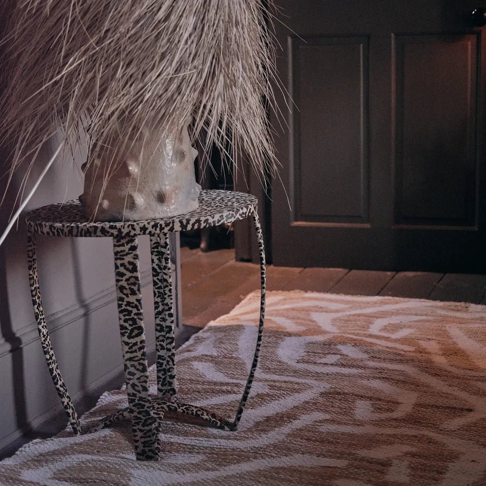Montgomery Chenille Jute Rug has cream and tan curved motifs across a textured surface, positioned beneath a narrow side table beside a dark panelled door.