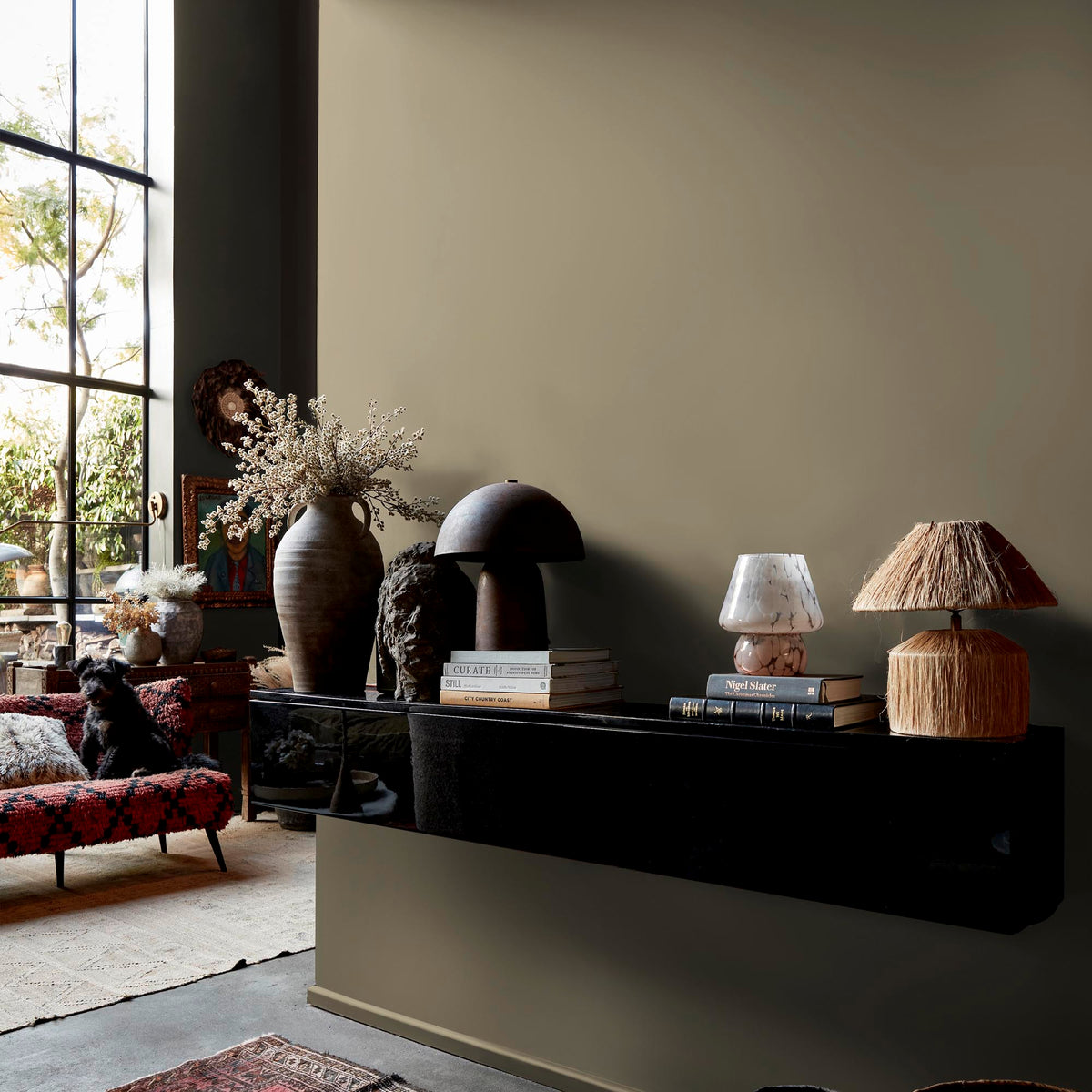 Abigail Ahern Moody Sage paint – a sumptuous neutral sage green enveloping a beautifully styled wall with mounted shelf, lamps and vases
