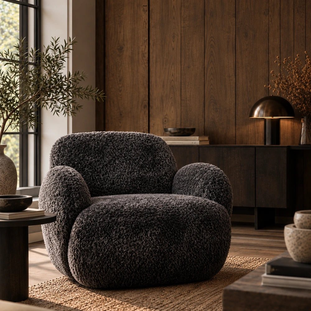 Natasha Faux Shearling Curved Armchair in charcoal with rounded plush upholstery, styled beside a dark side table in a warm neutral living room.