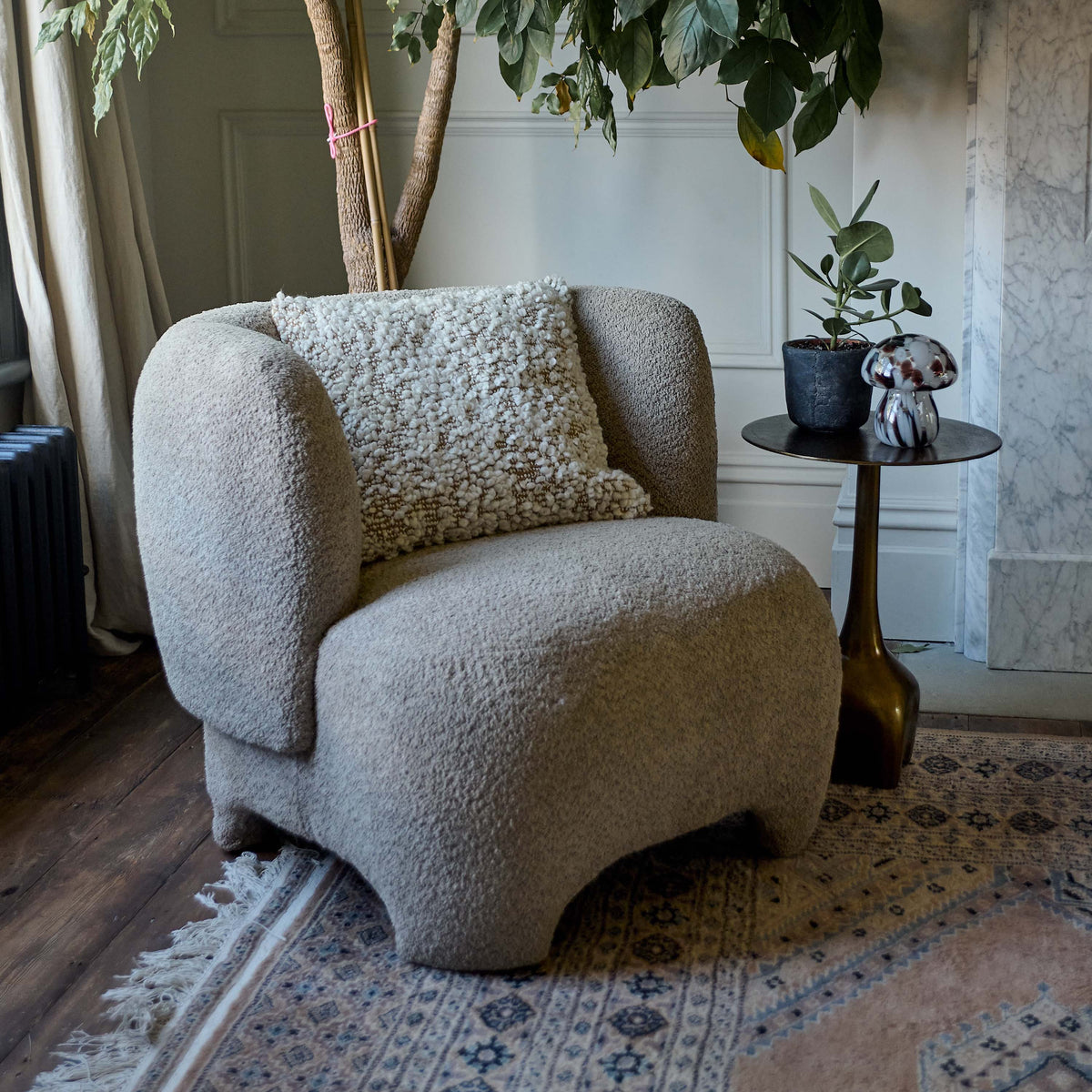 The Hallet Boucle Cushion, a square cushion in warm brown with cream boucle accents placed on a curved cream boucle armchair.
