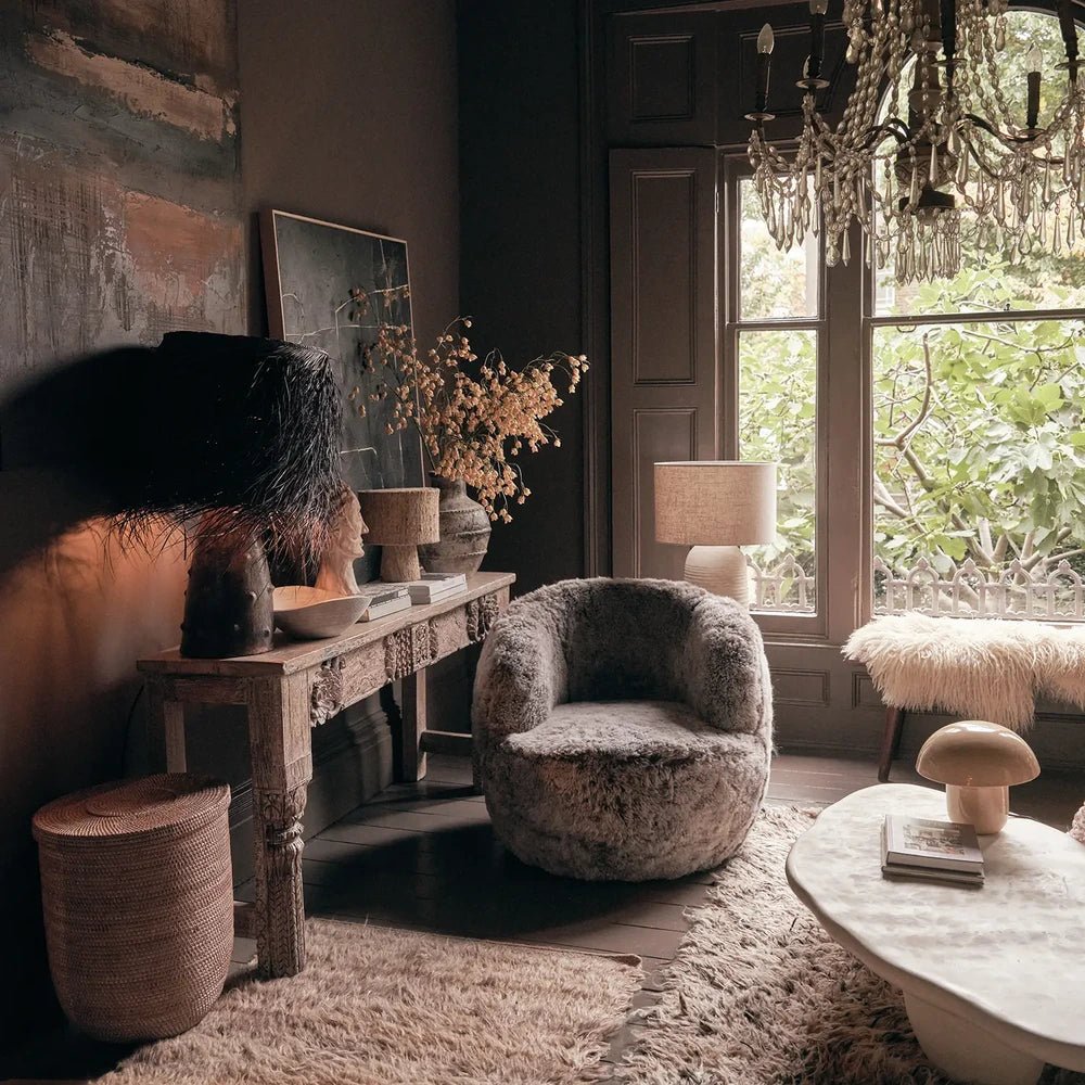 Norwood Sheepskin Swivel Chair has a rounded grey textured form, styled beside a console and circular coffee table in a living room with tall windows.