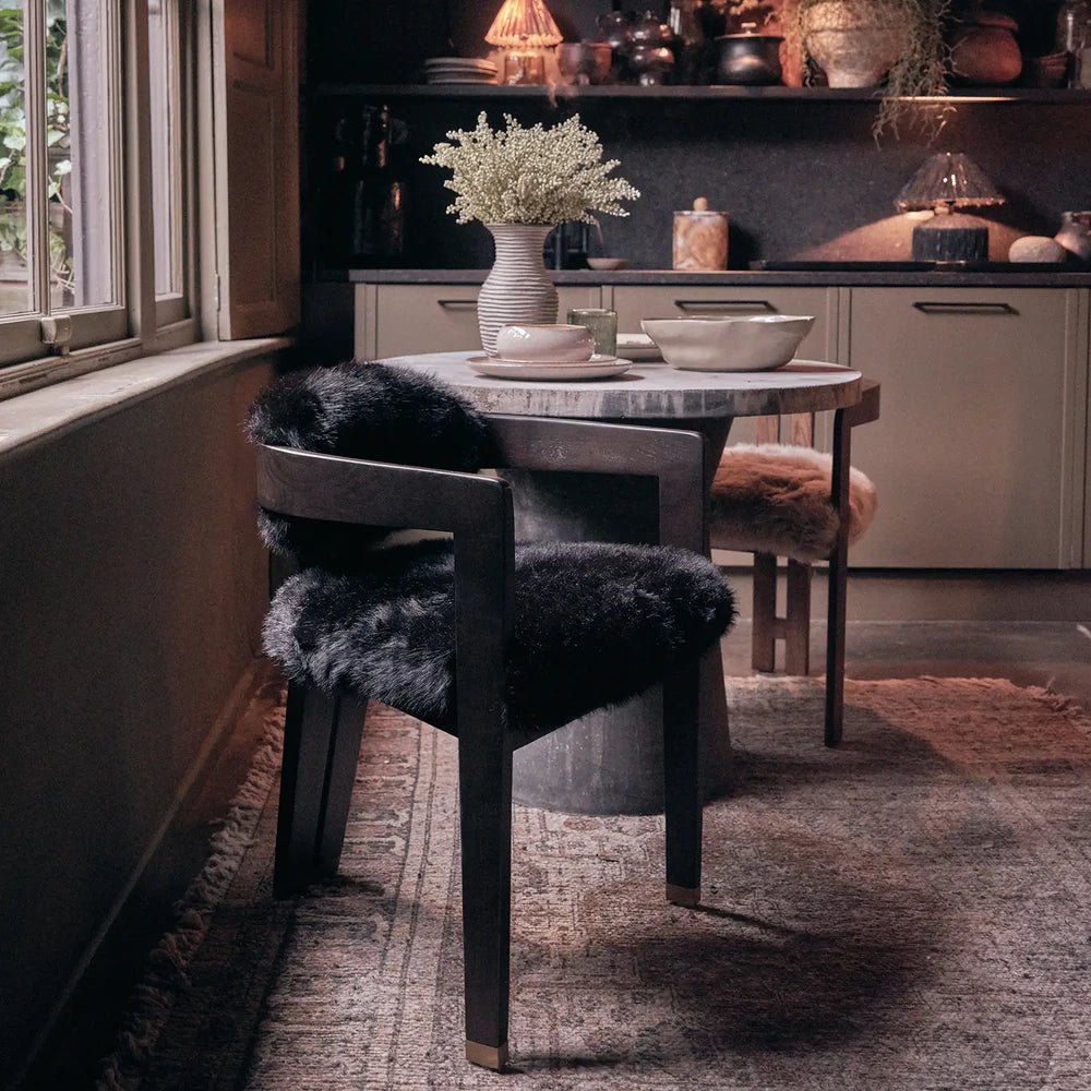 Norwyn Faux Fur Dining Chair combines black shaggy upholstery with a dark wooden frame, placed beside a dining table in a softly lit fireside room.