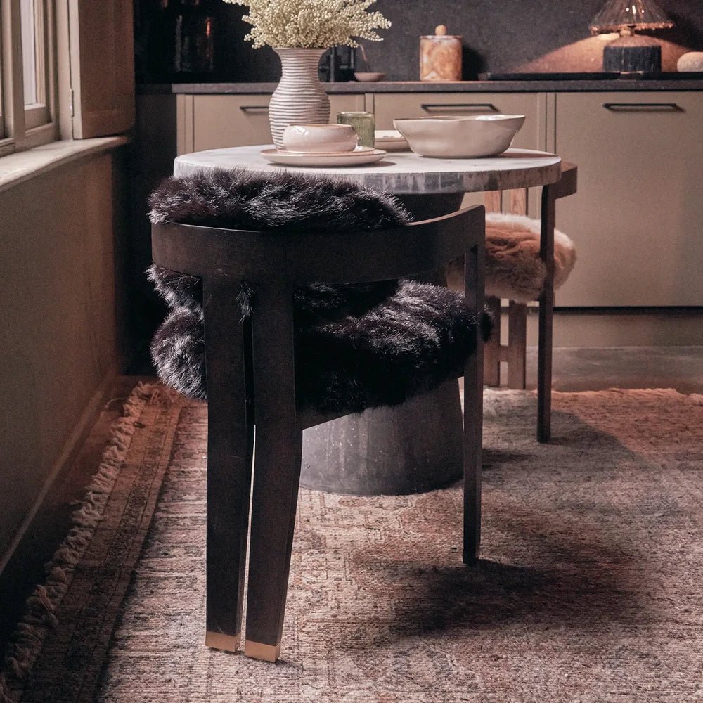 Norwyn Faux Fur Dining Chair reveals a dark wooden back rail and legs surrounding shaggy black upholstery, styled at a dining table near a fireplace.