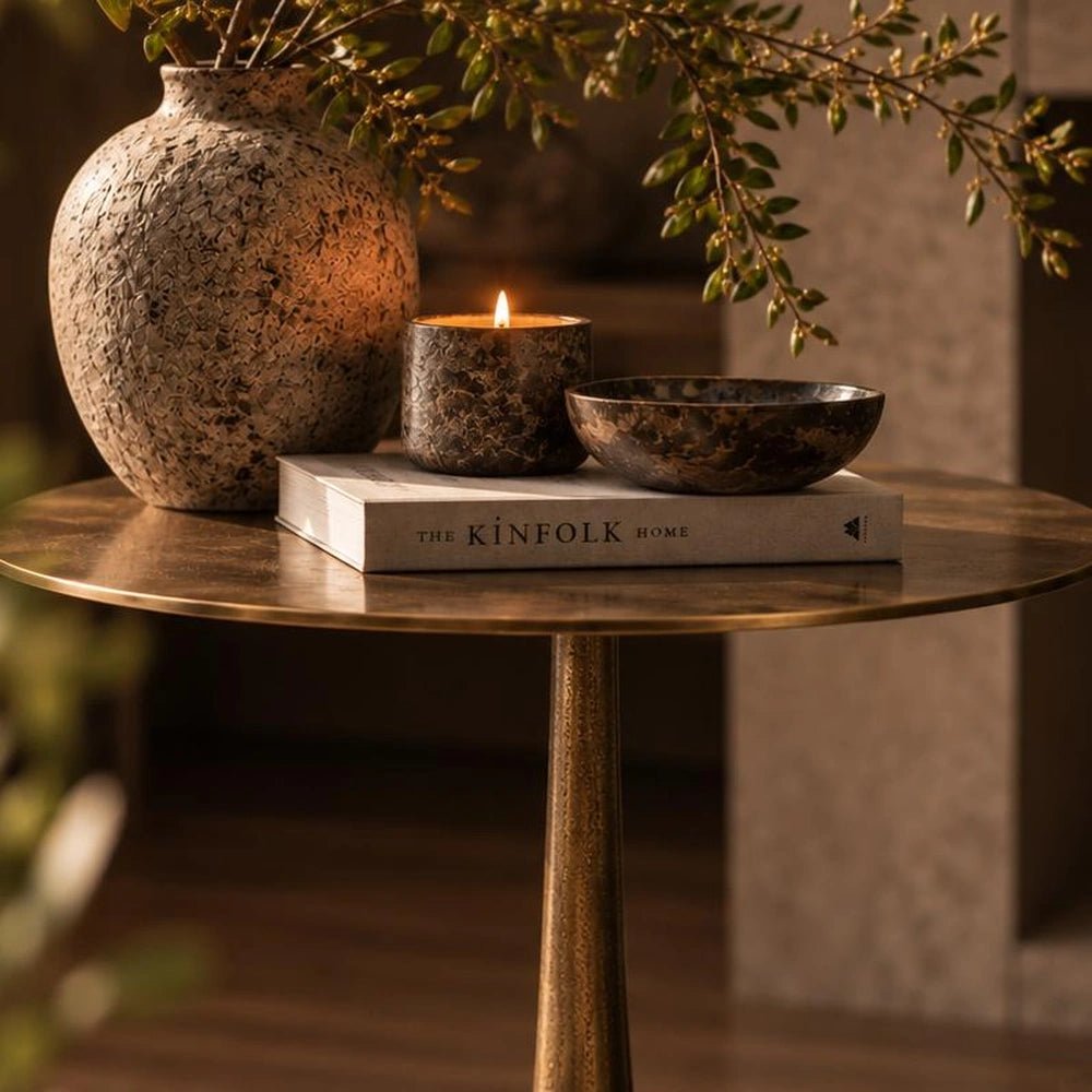 Oren Side Table in warm gold metal, styled beside a neutral sofa with layered cushions, decorative objects and rich contemporary interior textures.