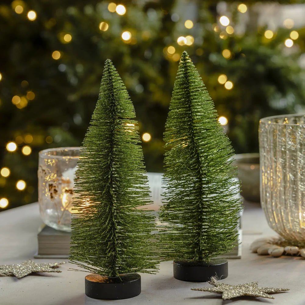 Orian medium green tree joins a trio of textured bottlebrush trees on dark bases, with candleholders and a star decoration creating a festive tabletop setting.