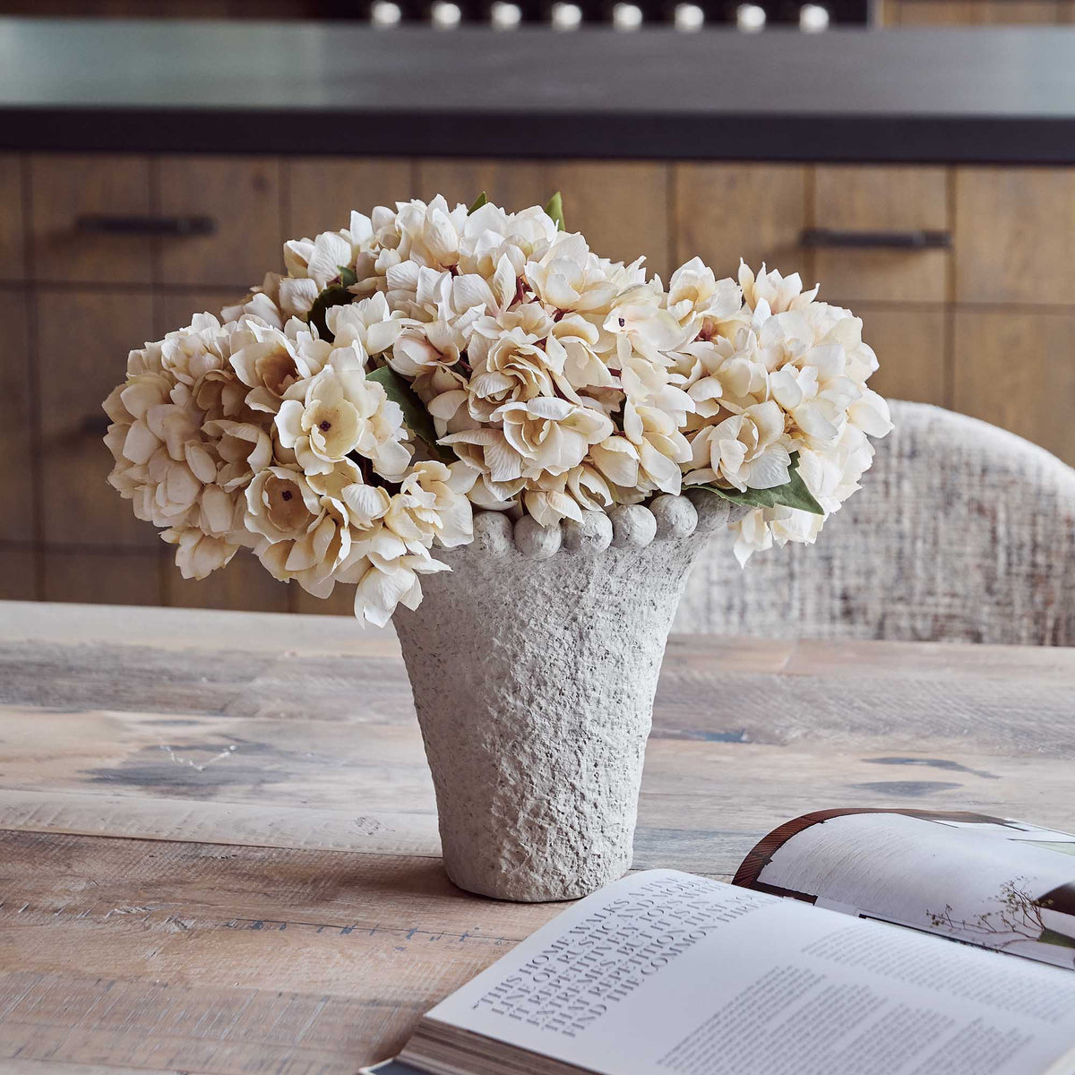 Vase with beige flowers on a wooden table with an open book