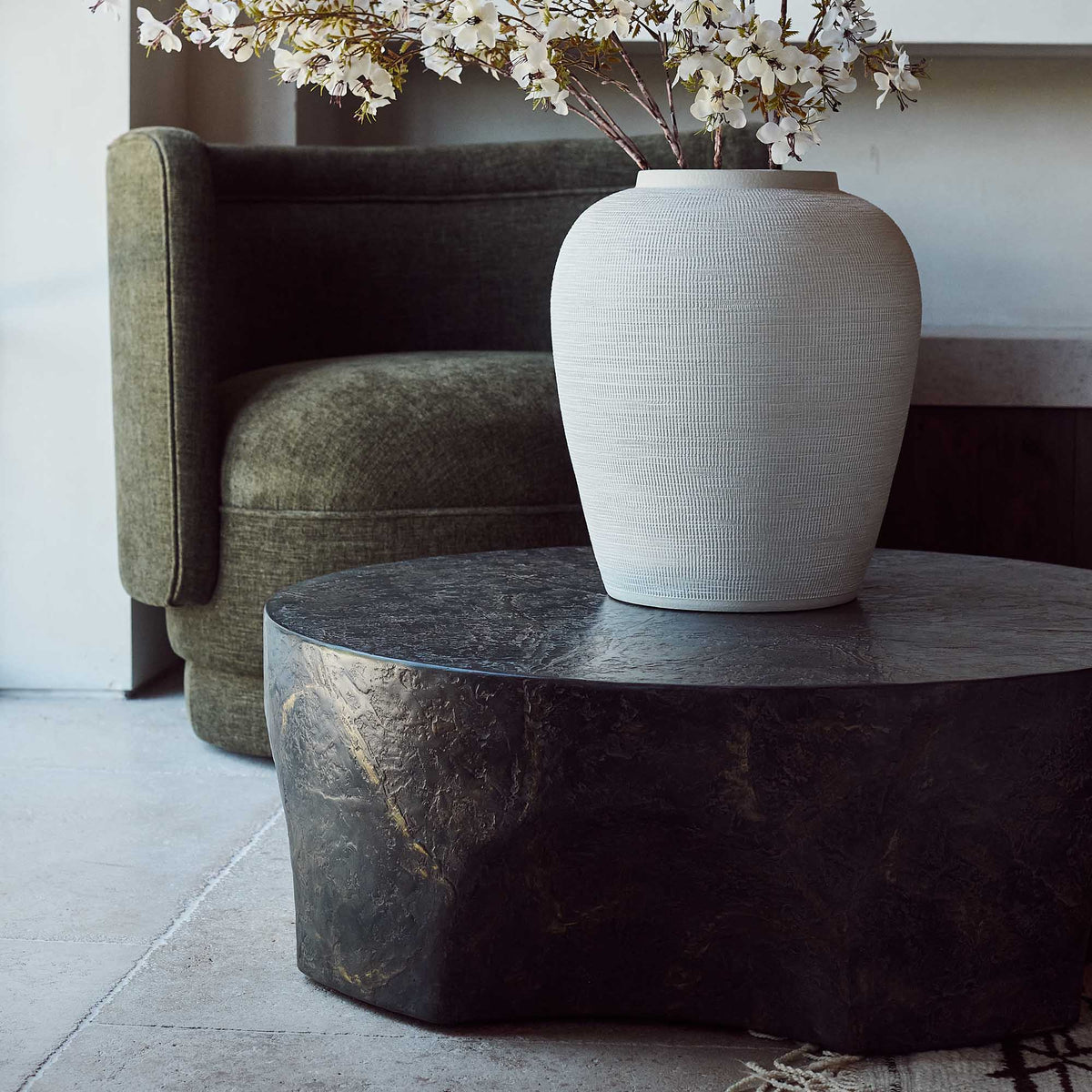 Close up of a Round concrete coffee table with a sculptural pinched base and rustic brown and slate grey finish. Pinch Round Coffee Table by Abigail Ahern, crafted from glass-reinforced concrete with a textured hand-painted effect, creating a luxury statement piece for modern living rooms, contemporary interiors and stylish outdoor spaces. A unique designer coffee table that adds natural texture, character and effortless sophistication to your home decor.
