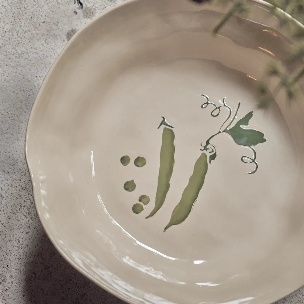Quincy Ceramic Bowl reveals a green pea pod illustration across its cream interior, with a glossy glaze and softly rippled rim visible in close-up.