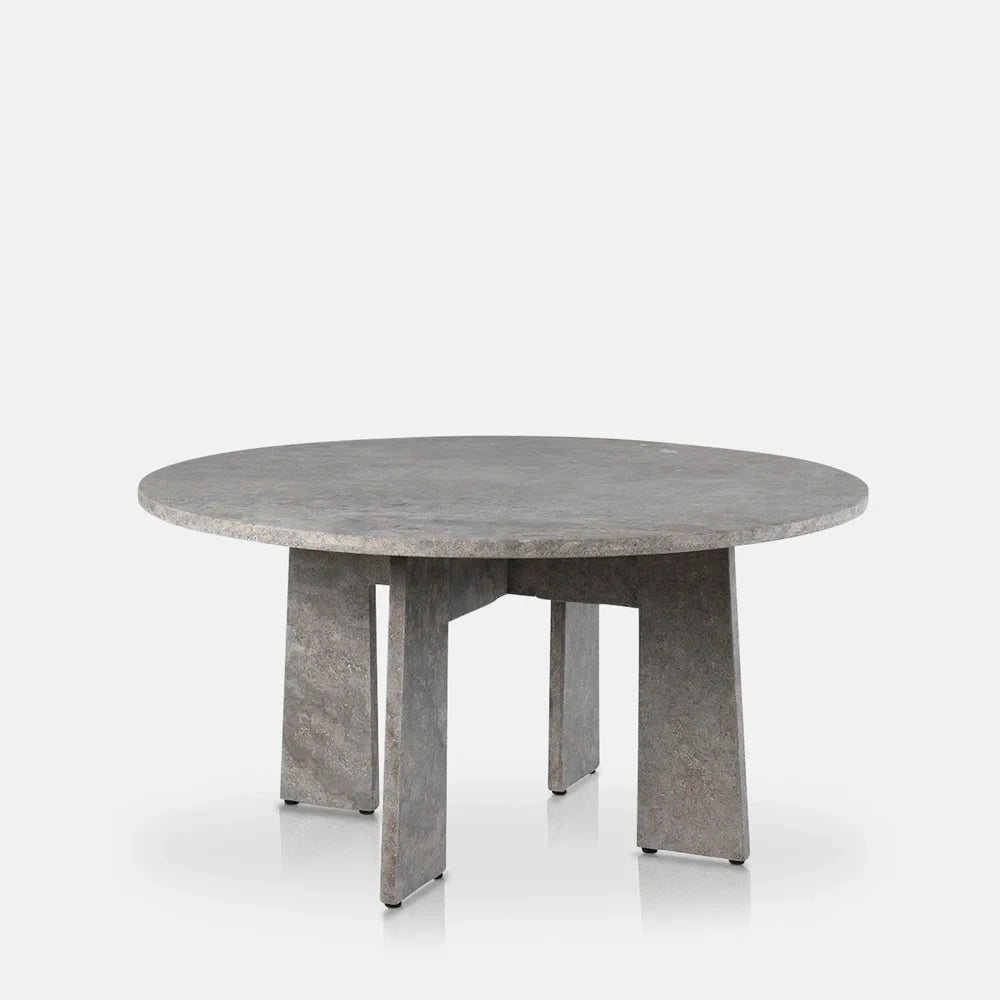 Randolph travertine dining table with a circular grey mottled top and intersecting angular slab legs, shown from the front to display its sculptural base.