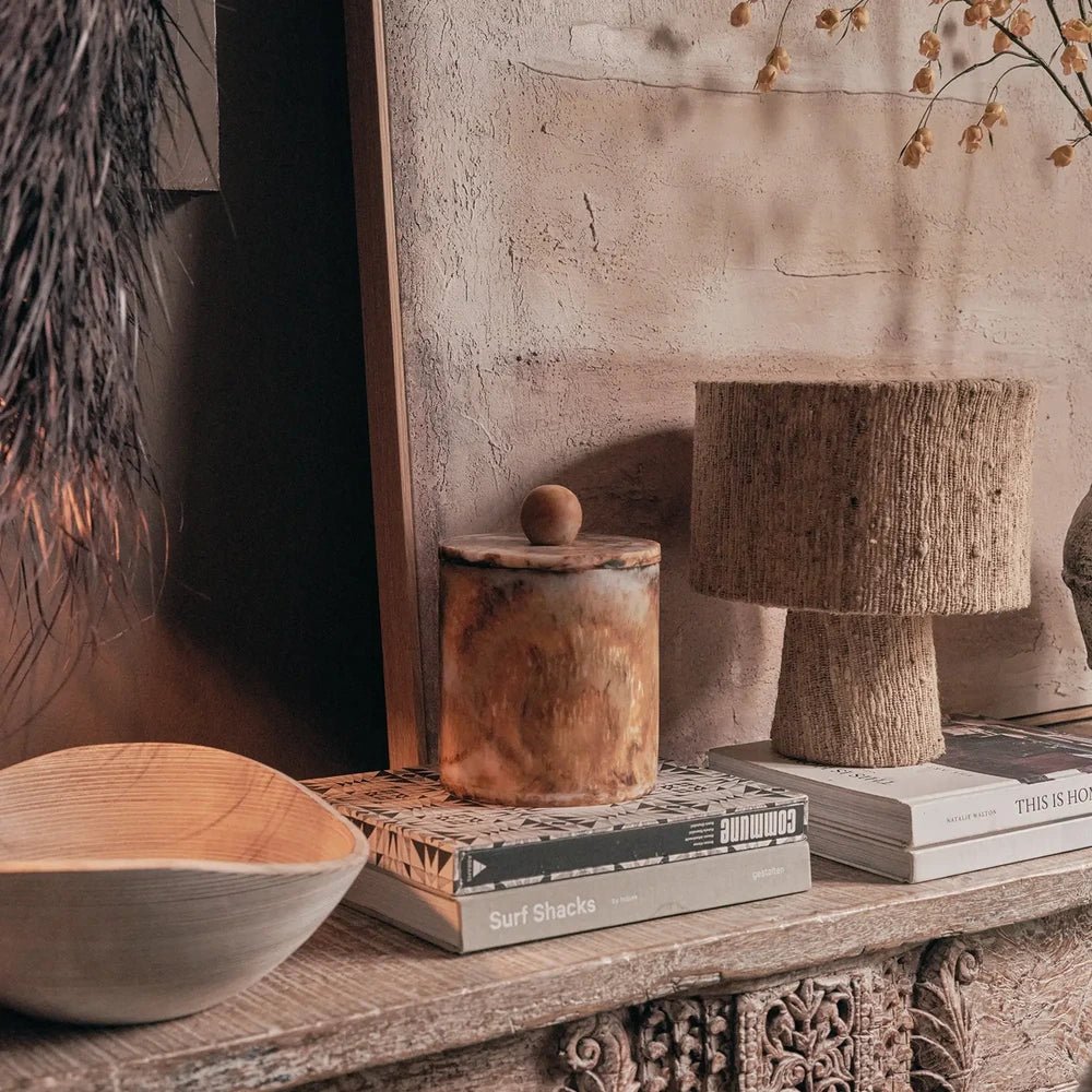 Reeve marble effect jar with a rounded lid knob and warm amber mottling, styled on stacked books beside a textured lamp on a console.