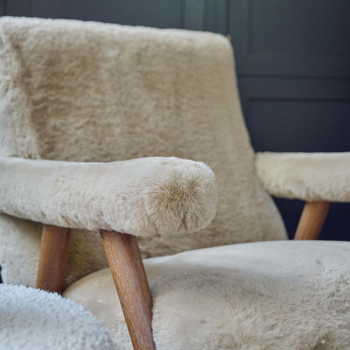 Close up of the The Robbins Faux Sheepskin Armchair, a super soft beige faux sheepskin armchair with padded armrests and a solid oak frame.