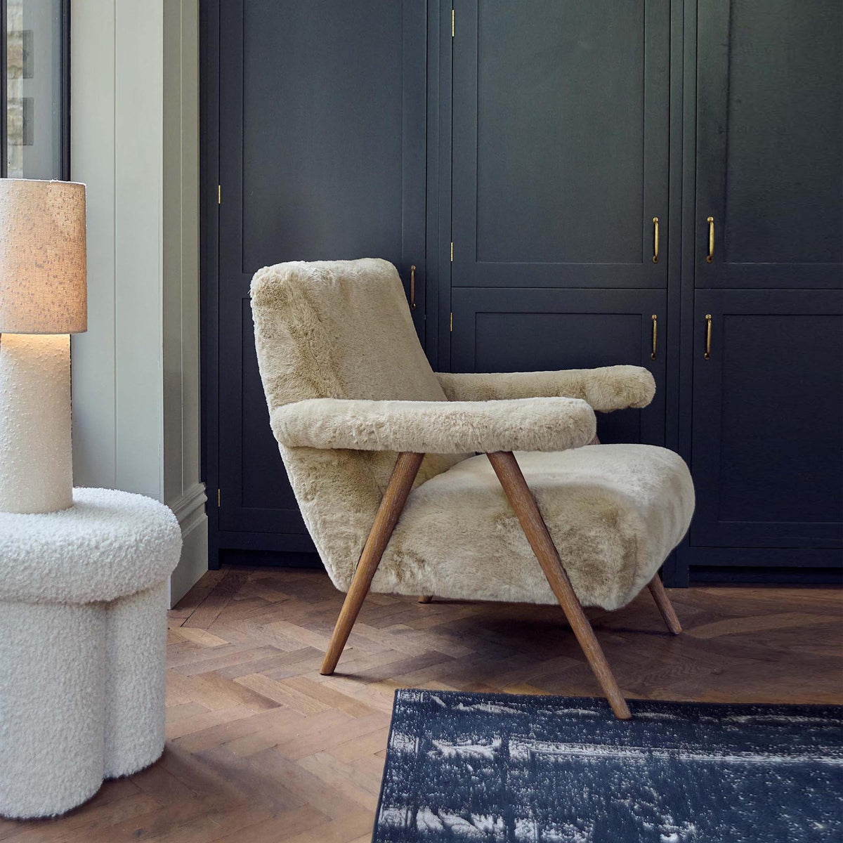 Beige faux sheepskin armchair with a soft textured upholstery, padded armrests and a timeless solid oak frame. Robbins Faux Sheepskin Armchair by Abigail Ahern, a luxury accent chair designed to bring warmth, comfort and natural elegance to modern living rooms, bedrooms and cosy reading corners. A statement piece of furniture perfect for creating a sophisticated, inviting and contemporary interior.