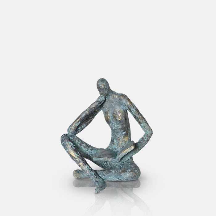 A cutout of the Rollo Figurative Sculpture, a faux brass polyresin sculpture in a blue tone of a seated figure reading a book.