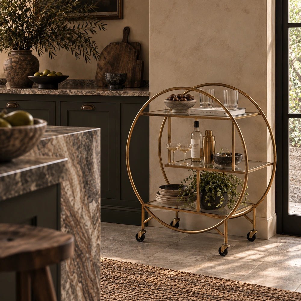 Rover Drinks Trolley with dark metal frame and glass shelves, styled with bottles and glassware in a warm contemporary room with layered accessories.