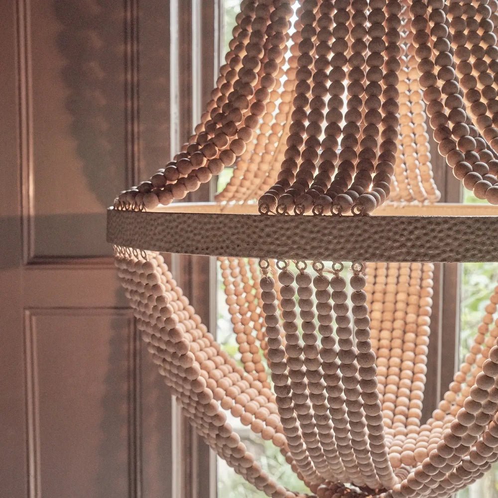Roxham beaded chandelier shown close up beside a window, revealing rows of rounded beads draped above and below a wide textured circular band.
