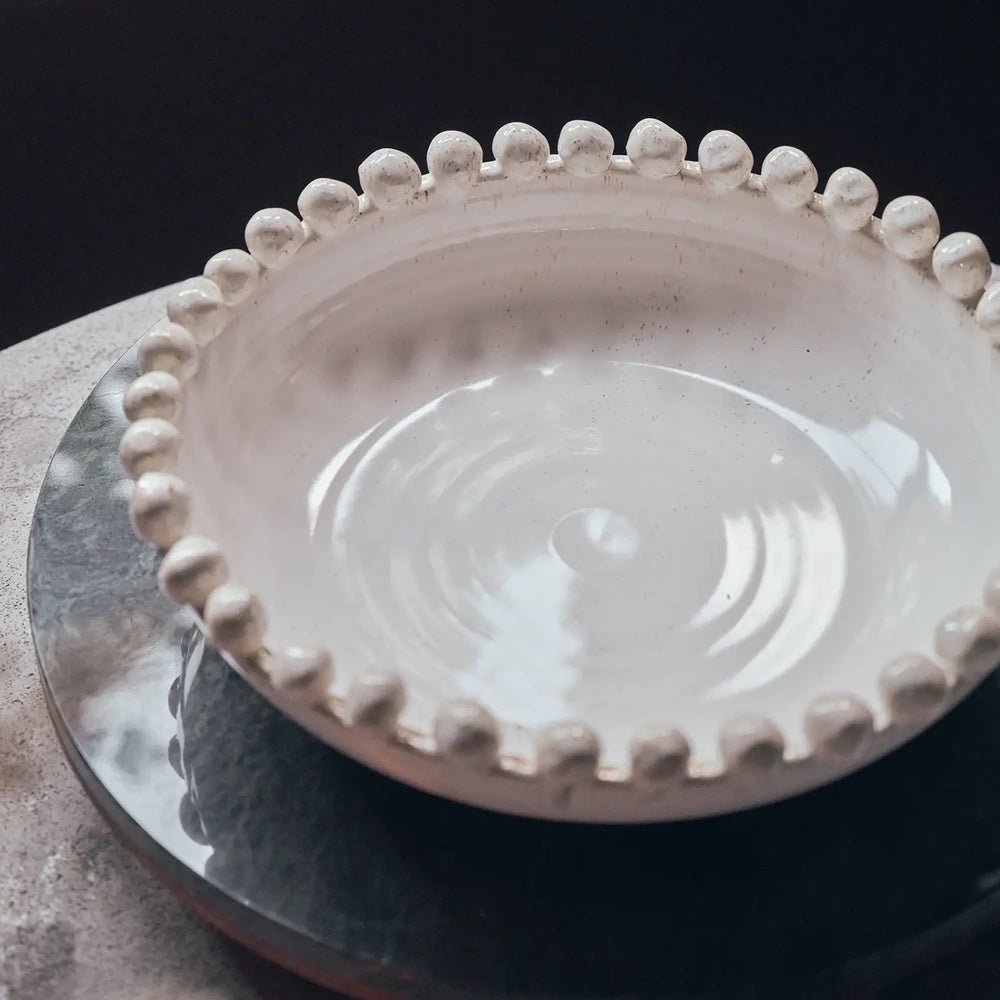 Rutledge bobble decorative bowl with a glossy pale interior and rounded beads along the rim, viewed from above on a dark round tray.