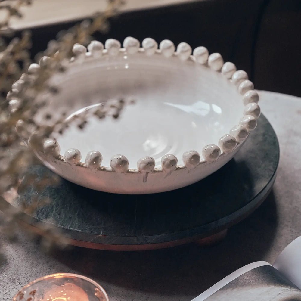 Rutledge bobble decorative bowl with a pale glazed interior and beaded rim, resting on a raised round tray beside a candle and open book.