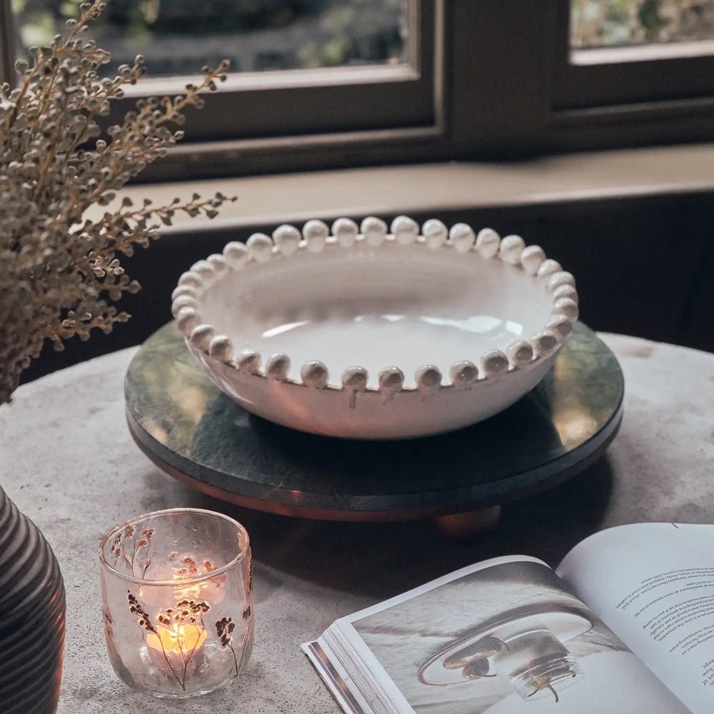 Rutledge bobble decorative bowl with a cream glazed interior and round rim details, styled on a coffee table tray near a window, candle and book.