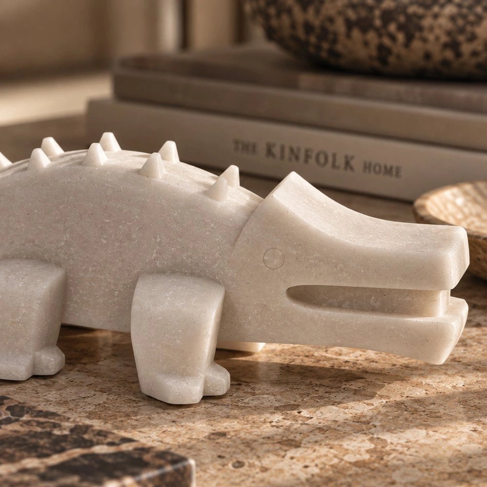 Salto Crocodile Sculpture displayed on a pale stone table beside stacked books and decorative objects, adding a small dark sculptural accent to the interior.