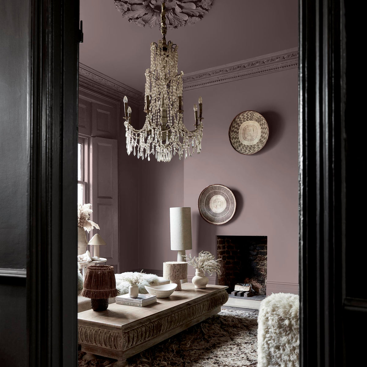 A living room with a glass chandelier hanging above a coffee table, with the walls painted in a warm, dusky purple paint colour.