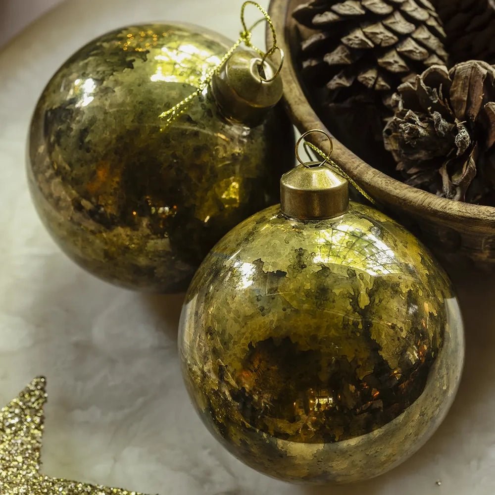 Silas antique gold baubles have rounded shapes and mottled reflective surfaces, displayed beside pine cones with gold hanging caps and a glittering star nearby.