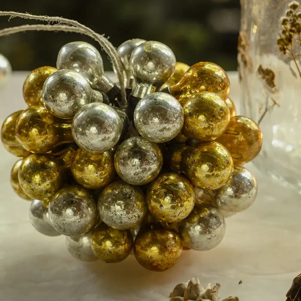 Silvero glass bauble shows reflective gold and silver spheres gathered into a rounded cluster, with a rustic hanging cord visible above its textured surface.