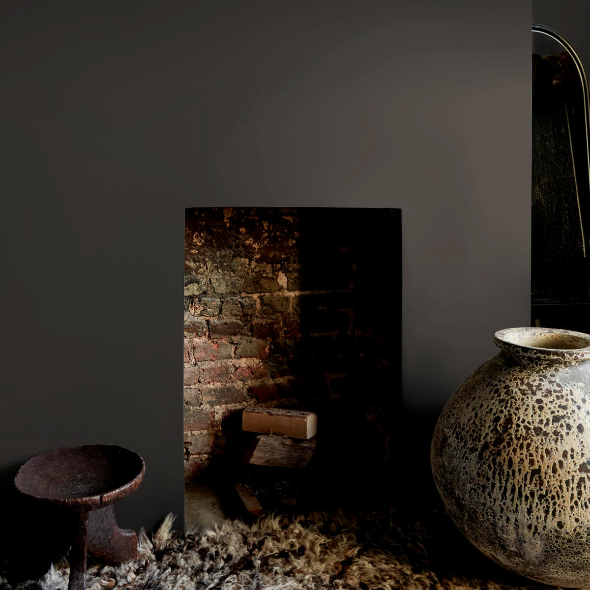 Abigail Ahern Smoky River paint – a sumptuous warm dark grey enveloping a beautifully minimalist fireplace setting with a statement ceramic vase
