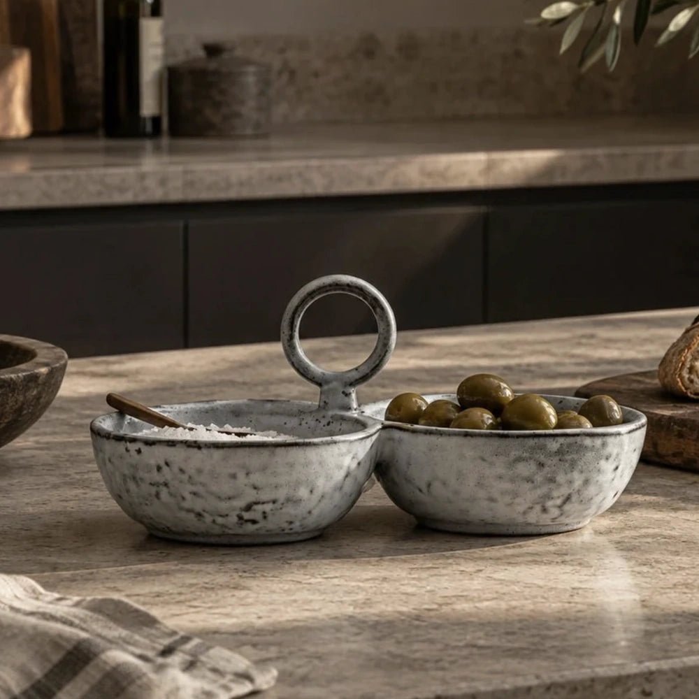 Somerton Ceramic Serving Bowls on a stone tabletop, showing the speckled glazed finish, linked bowl design, metal ring handle and olives in a styled kitchen.