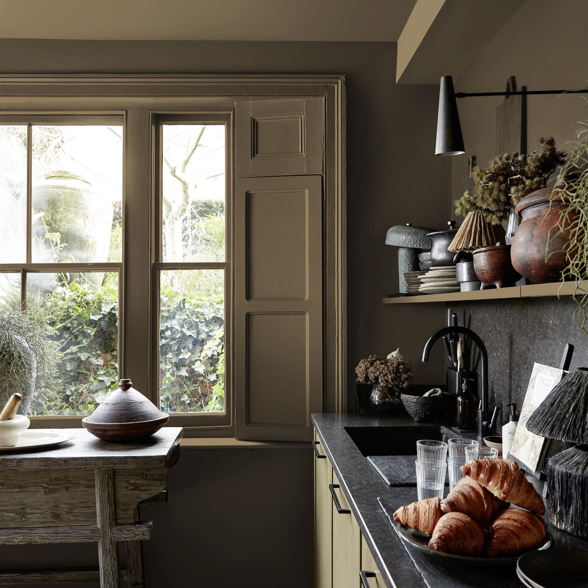 A kitchen window shutter and wall painted a warm brown paint colour with a Abigail Ahern Summer Earth paint – a sumptuous warm brown with golden undertones enveloping a beautifully styled kitchen window shutter and wallgolden undertone.
