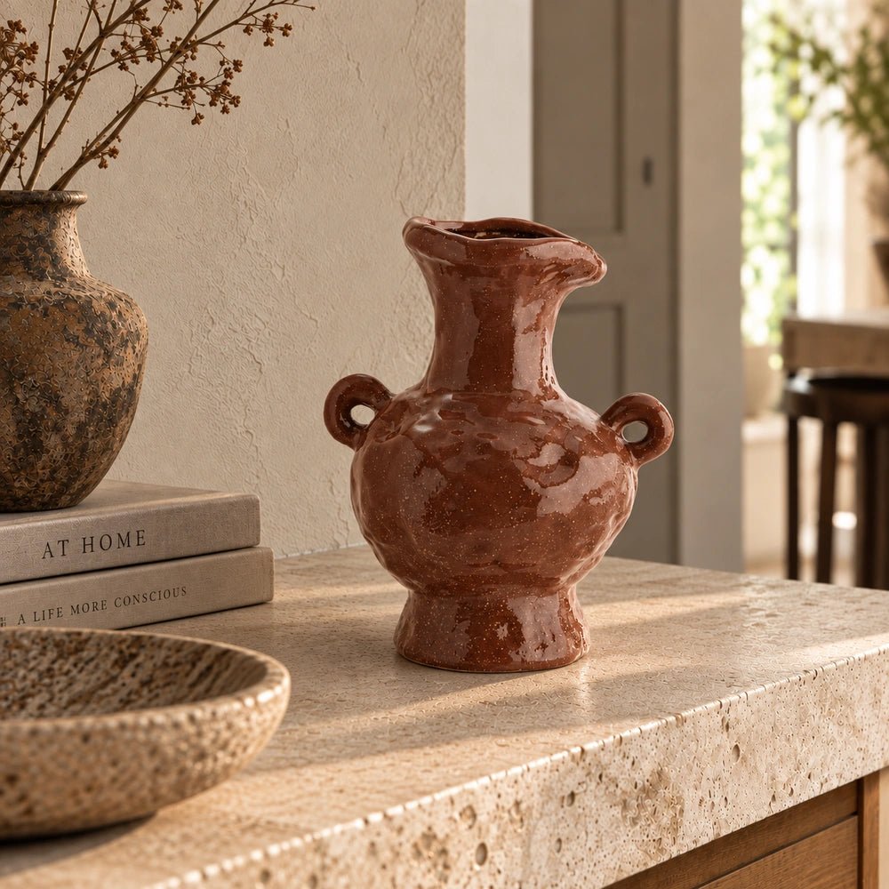 Sylvan Stoneware Vase with sculptural handles and glossy brown finish, displayed on a pale stone console beside stacked books, a decorative bowl and dried stems.