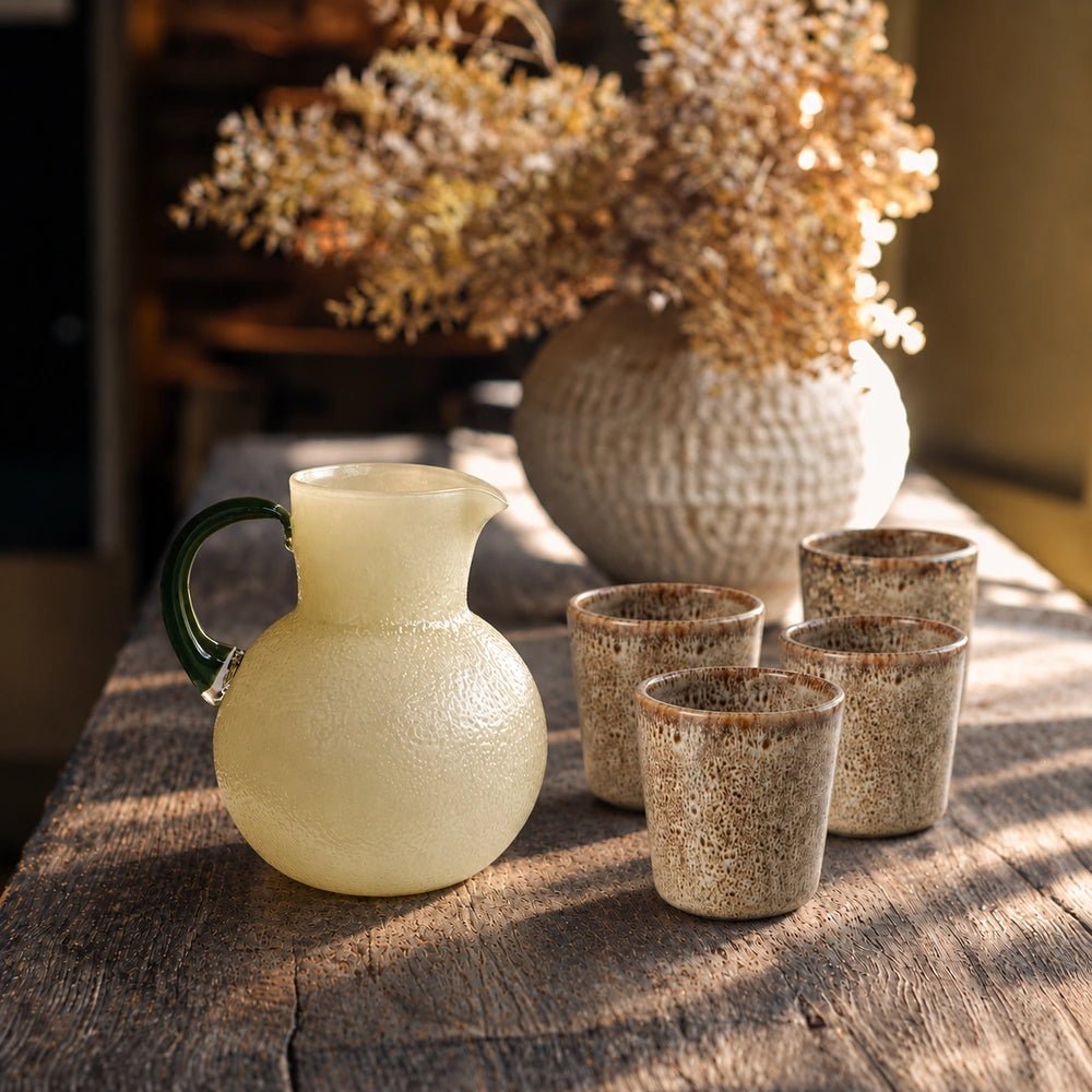Tisbury Porcelain Cup, Set of 4 grouped on a sunlit table, showing speckled neutral ceramic surfaces beside a pale jug and textured vase.