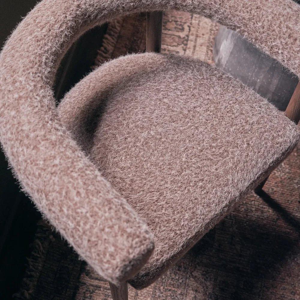 Virgil upholstered dining chair shown close up from above, highlighting the taupe textured fabric, rounded seat cushion, curved padded arms and slim dark frame.