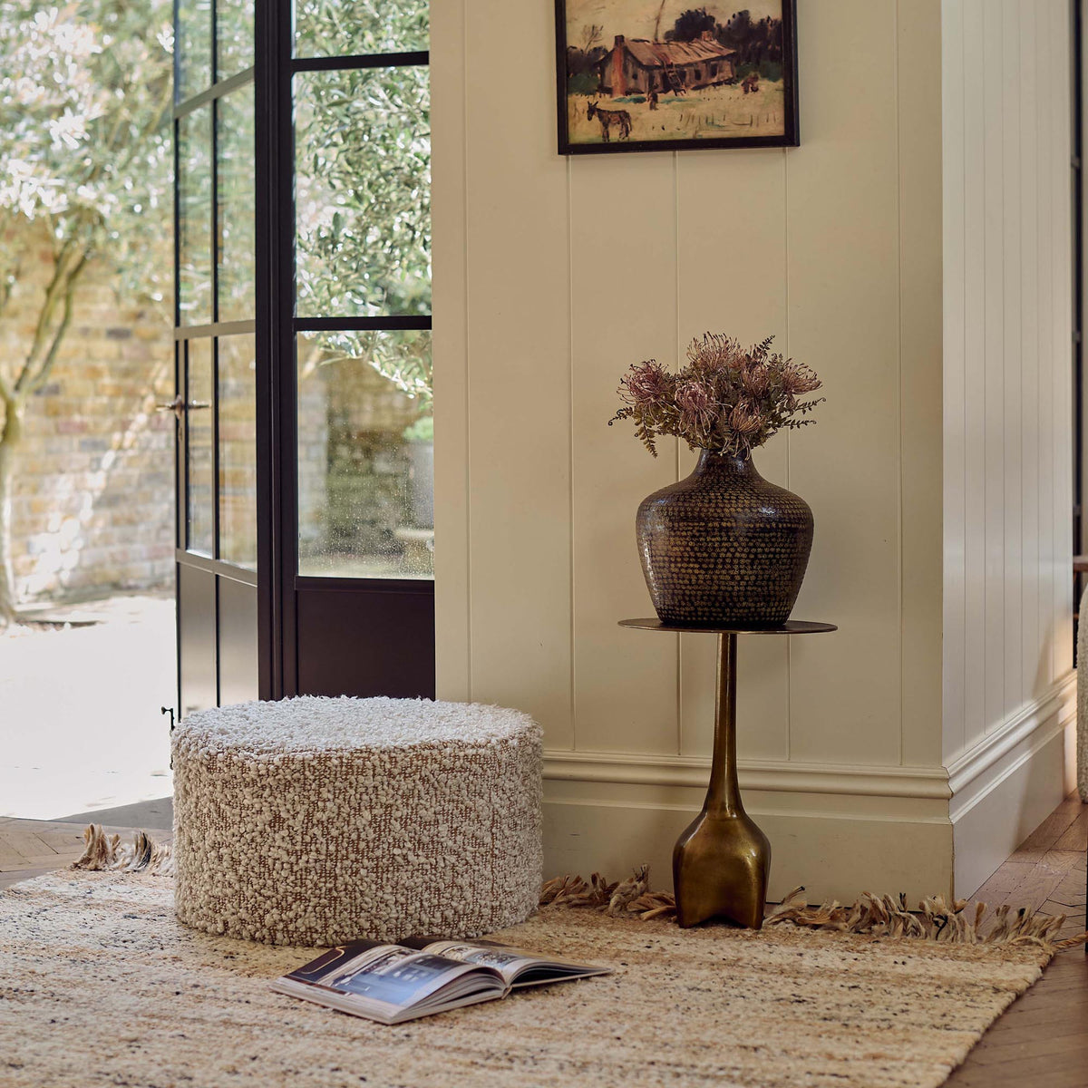 The Walker Boucle Pouffe, a circular puffe in warm brown with cream boucle accents in a bright sunny lounge room.