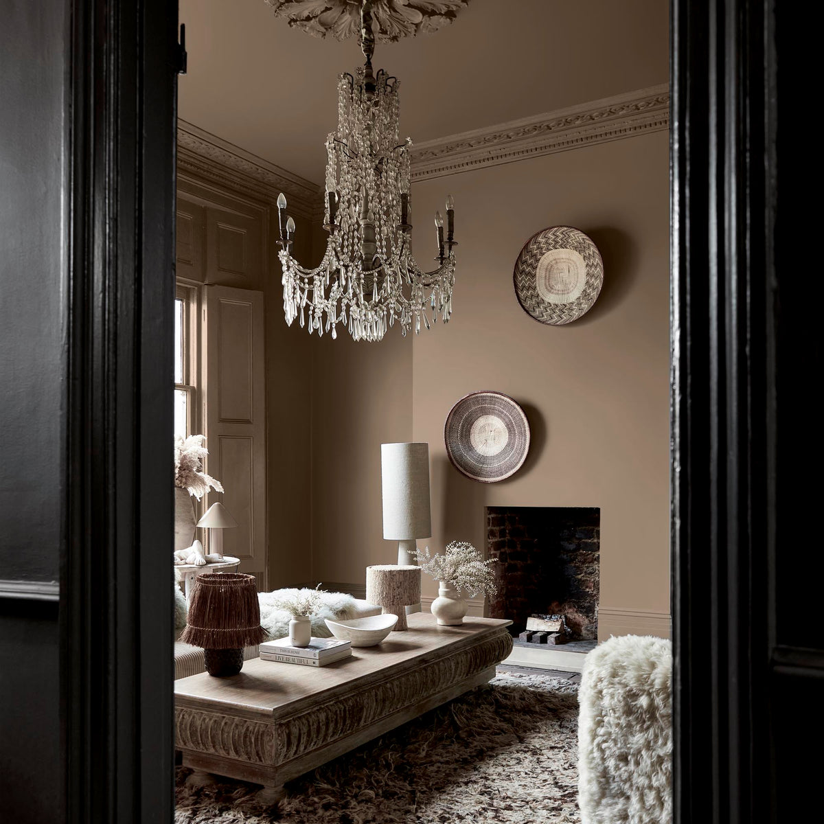 Abigail Ahern Weathered Linen paint – a sumptuous warm brown with golden undertones enveloping a beautifully styled living room beneath a statement glass chandelier