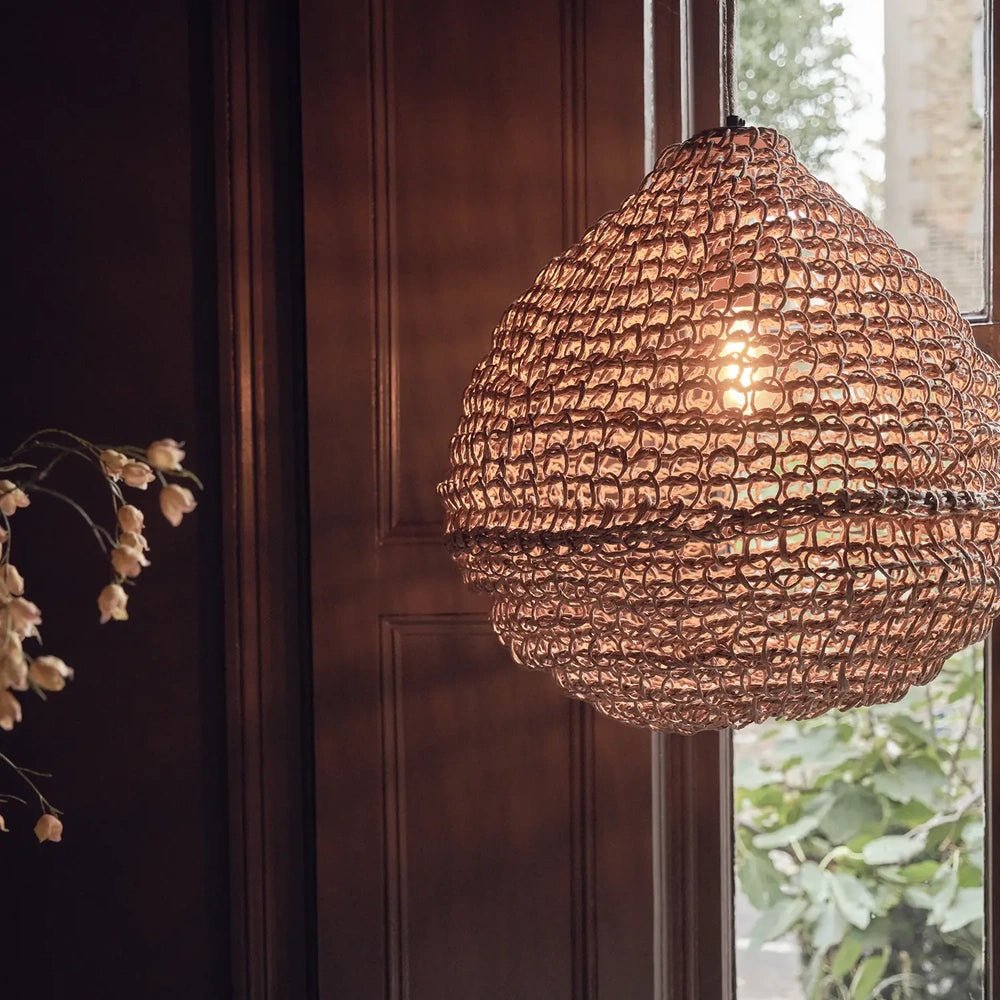 Westcott paper rope pendant glows beside a window, its rounded woven brown shade casting warm light through the open texture against dark wooden panelling.