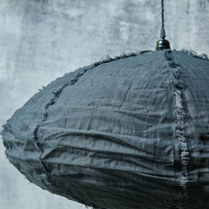 Black oval shaped fabric pendant shade hanging from a black cord against a concrete background.