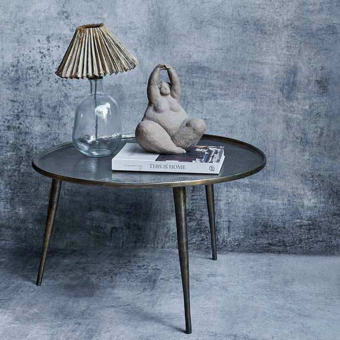 Clear glass lamp with raffia shade placed on a large round coffee table next to a sculpture