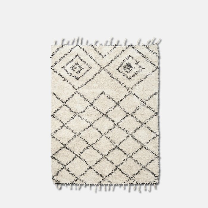 A cutout of the Keoni Rug, a rectangular soft cream fringed rug with a black diamond design in a Berber style.