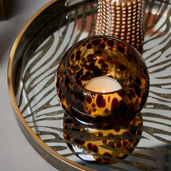 Brown glass candleholder sitting on a round mirrored zebra-pattern tray.