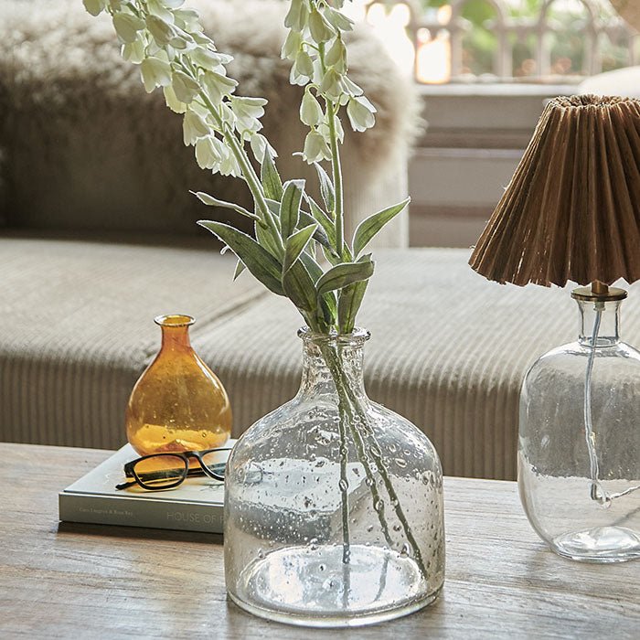 Artificial flowers in a curved clear glass bottle vase.