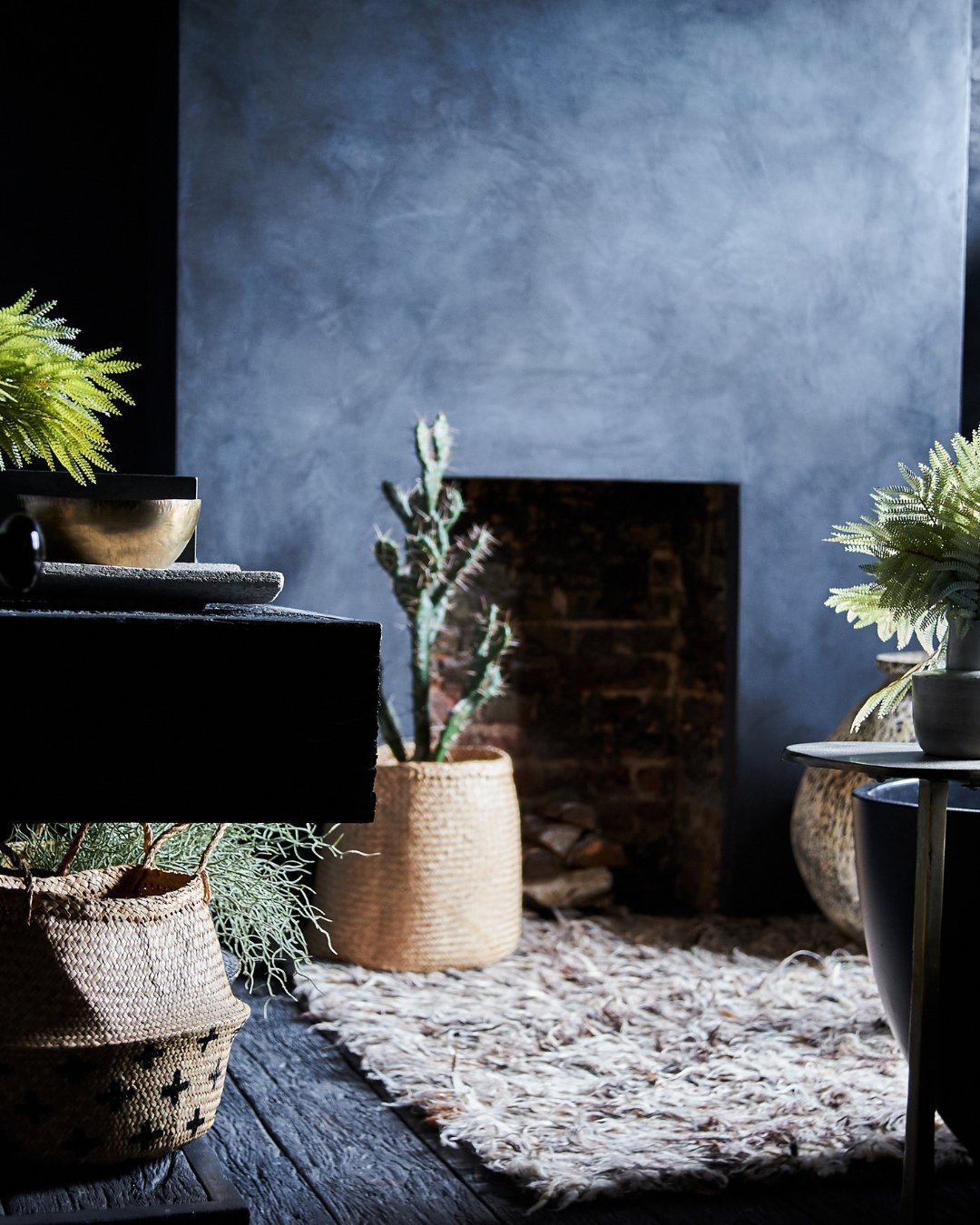 A stylish bathroom with dark tadelakt walls, plants in baskets and a shaggy wool rug.