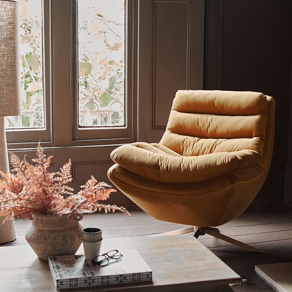 A dark yellow velvet retro design accent chair with a vase of artificial fern leaves in the home of designer Abigail Ahern